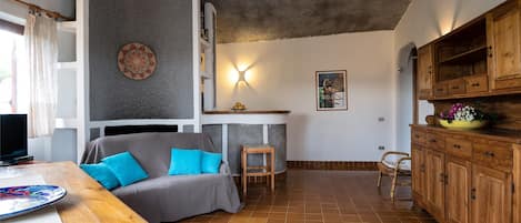 Een gezellige woonkamer met een grijze bank, een houten eettafel en een keuken met houten kastjes.