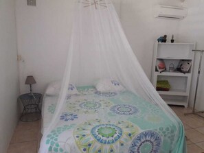 Una cama con dosel, una mesita de noche con lámpara, y una estantería con diversos objetos.