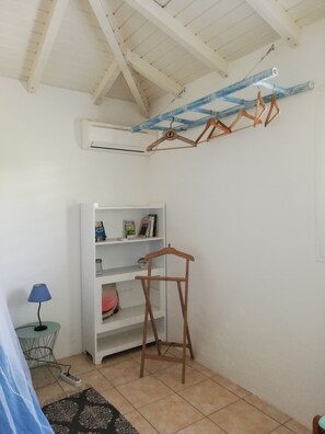 Una habitación con una estantería blanca, una lámpara azul, un perchero de madera y un suelo de baldosas.
