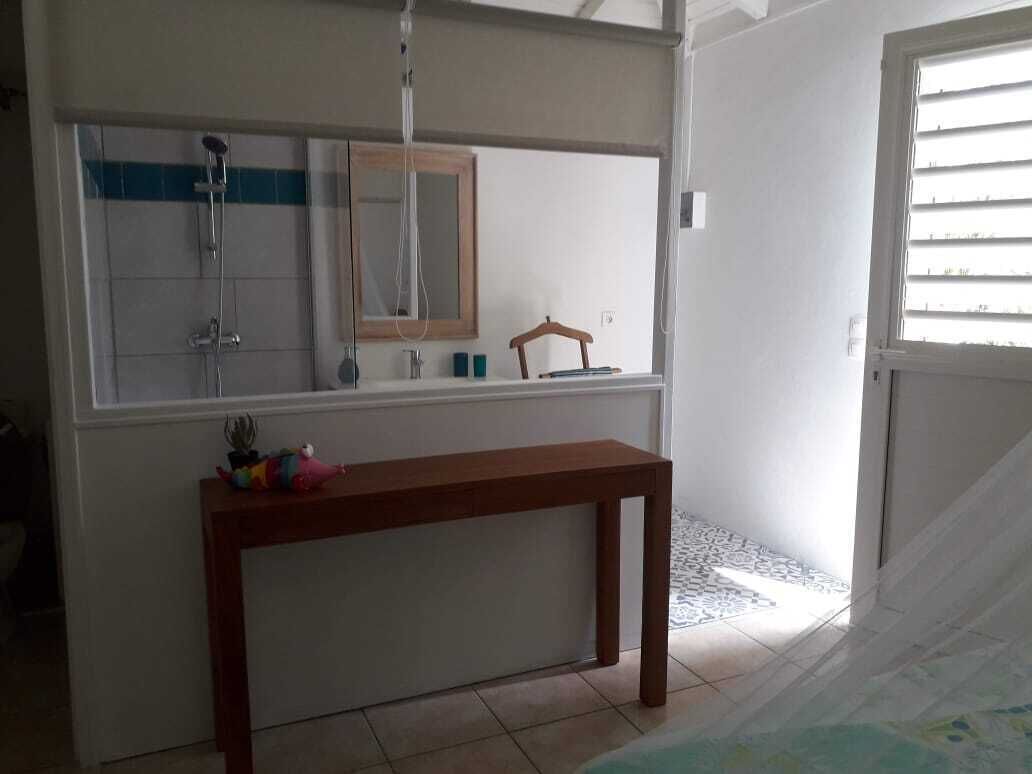 A bathroom with a shower, a mirror, a wooden bench, and a window with blinds.