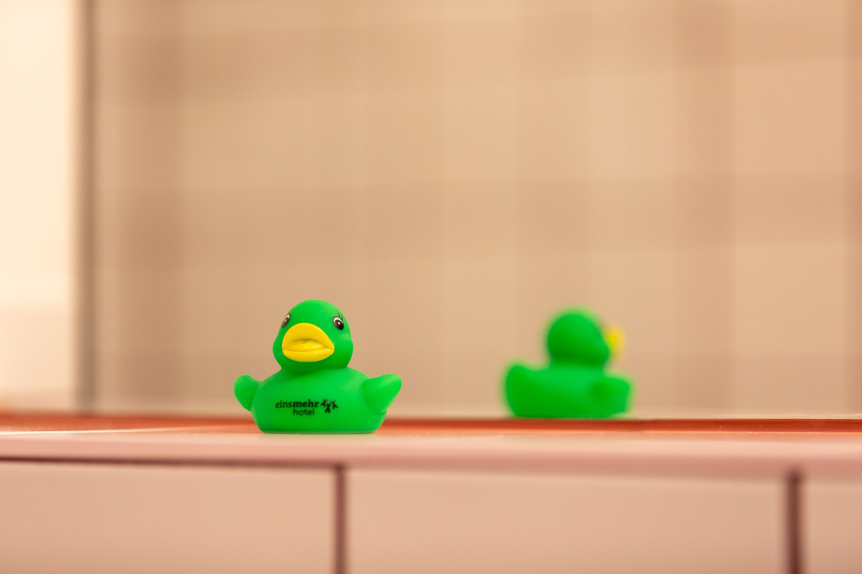 A bathroom with a green rubber duck and a green rubber ducky on a tiled surface.