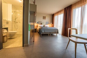 A hotel room with a shower, toilet, bed, and a dining area.