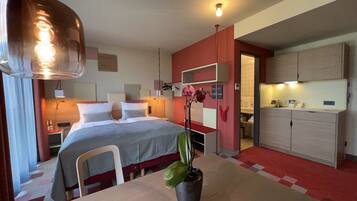 Een moderne hotelkamer met een bed, nachtkastjes, een bureau, een eettafel en een keukenhoek.