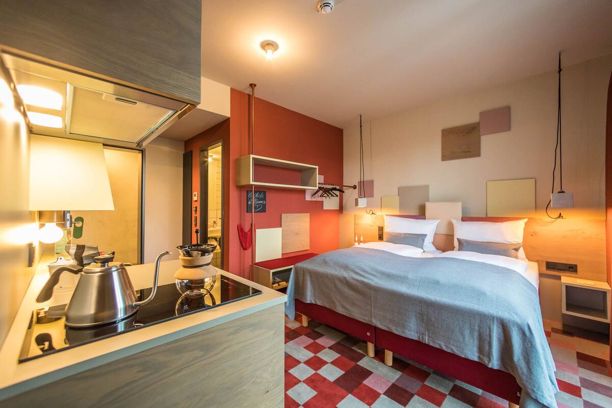 Une chambre d’hôtel comprenant un lit, des tables de chevet, un bureau avec une bouilloire et un miroir.