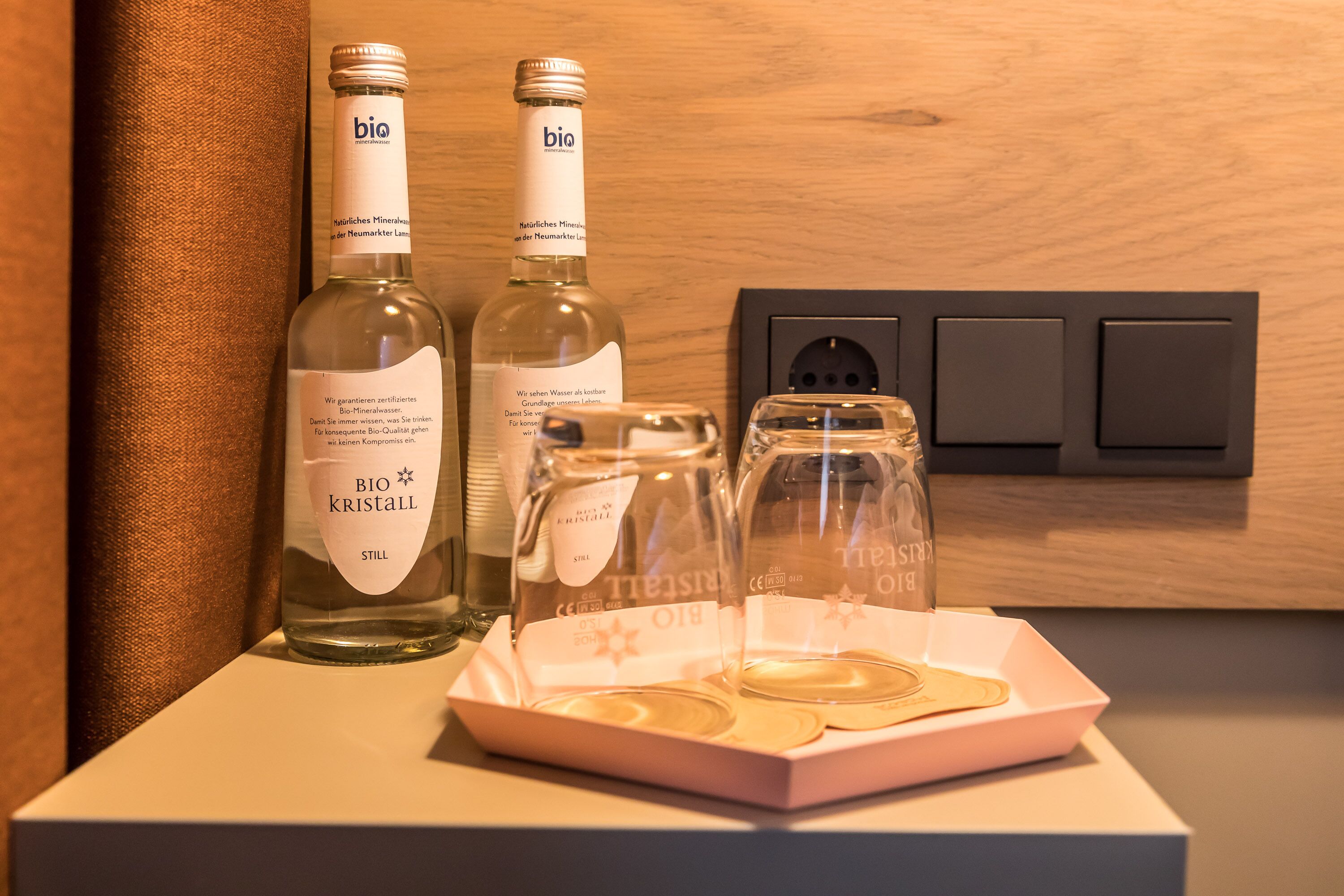 Two bottles of bio kristall still wine and a glass decanter on a white surface.