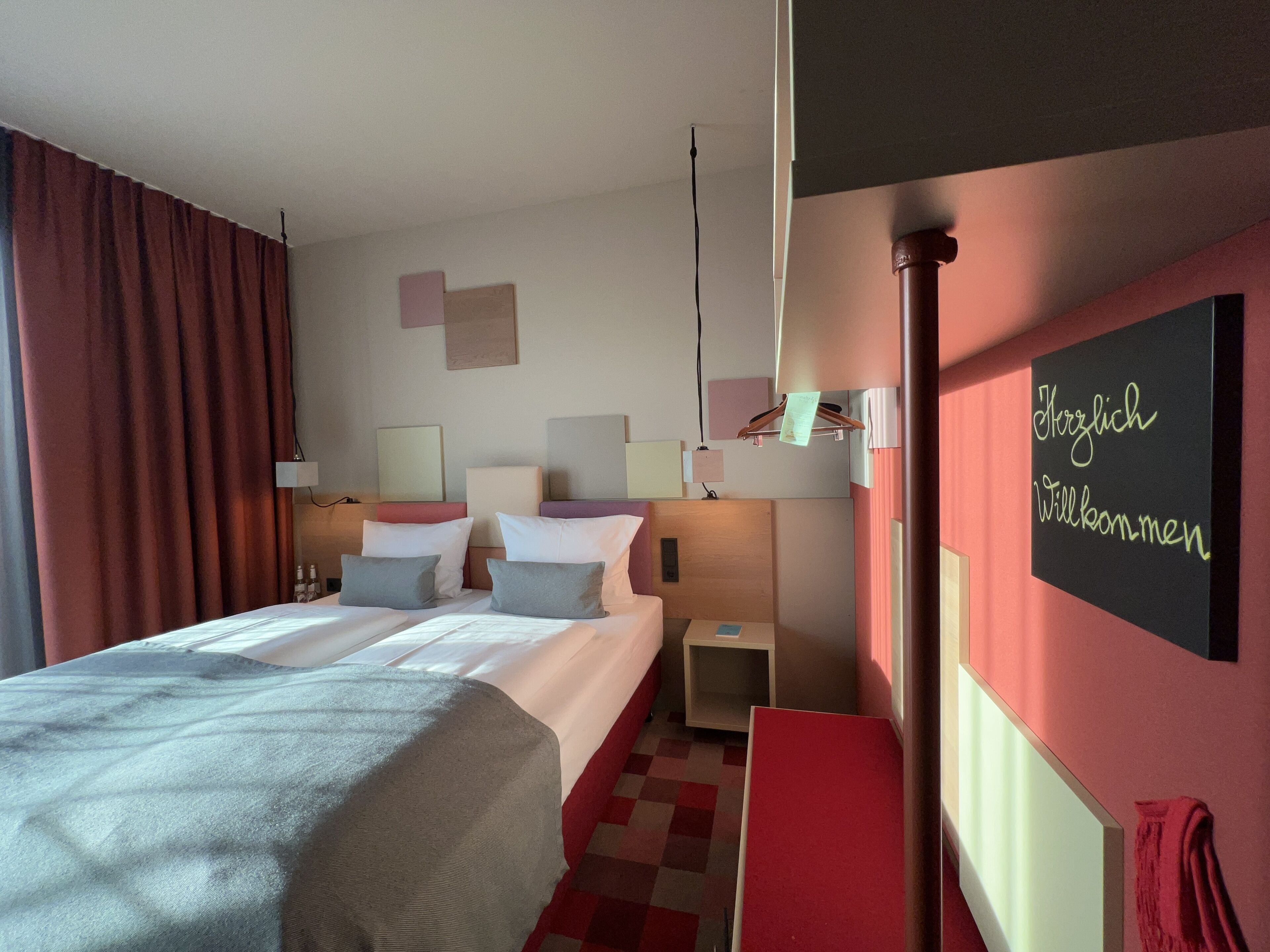 A hotel room with two beds, a bedside table, a nightstand, and a wall-mounted shelf.
