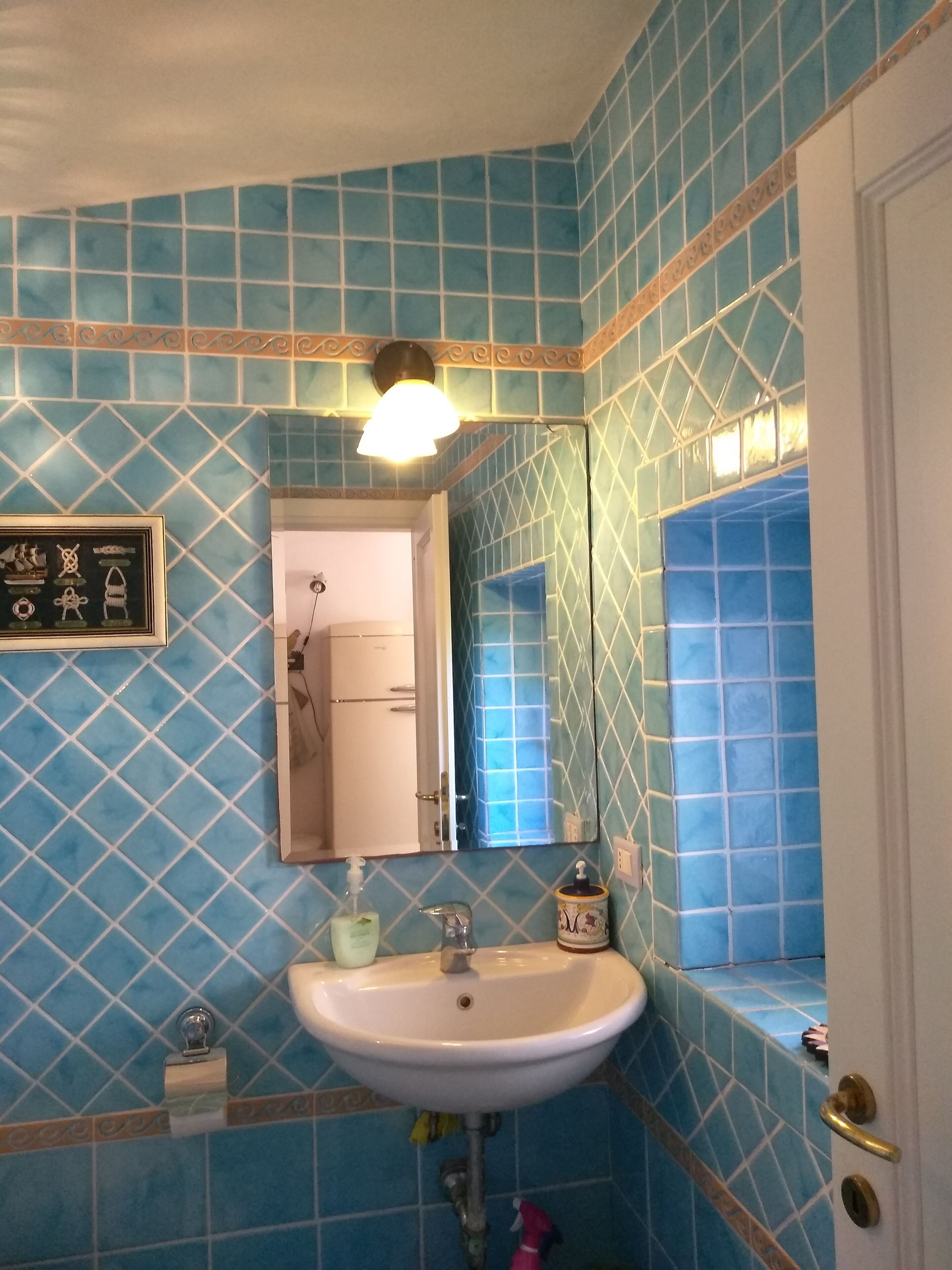 A bathroom with blue patterned tiles, a white sink, a mirror, and a framed picture on the wall.