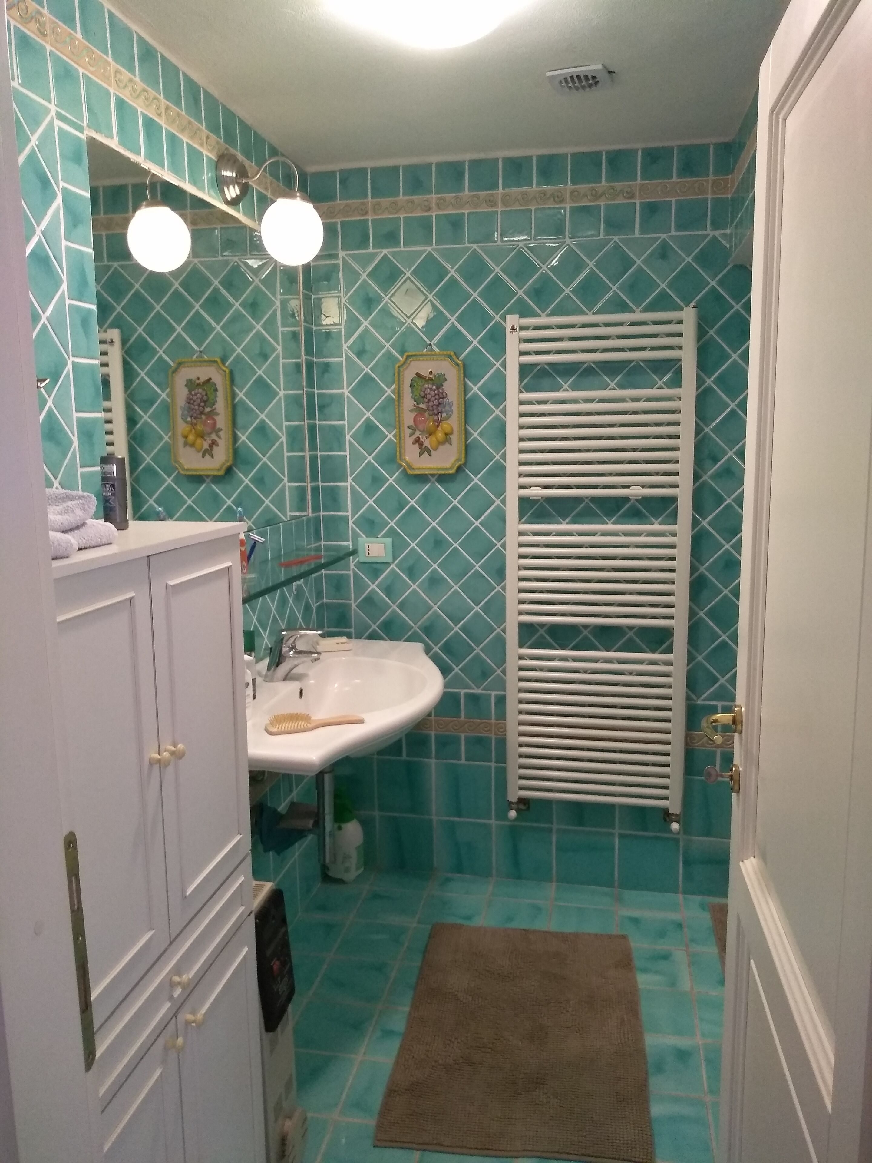 A bathroom with a white sink, a mirror, and a towel rack. There is a white radiator and a brown rug on the floor.