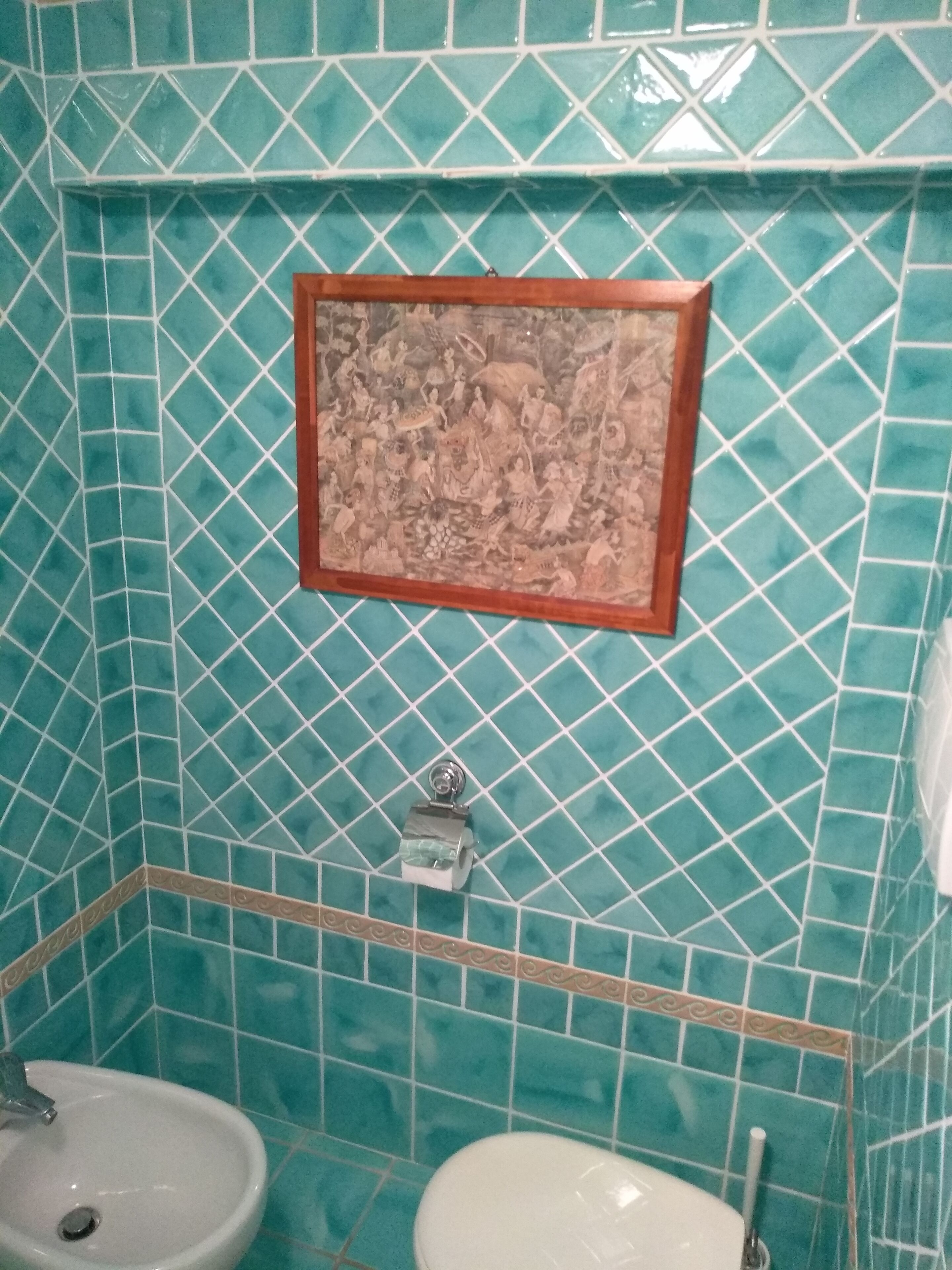 Ein Badezimmer mit türkisfarbenen Mosaikfliesen, einem gerahmten Bild an der Wand und zwei Waschbecken.