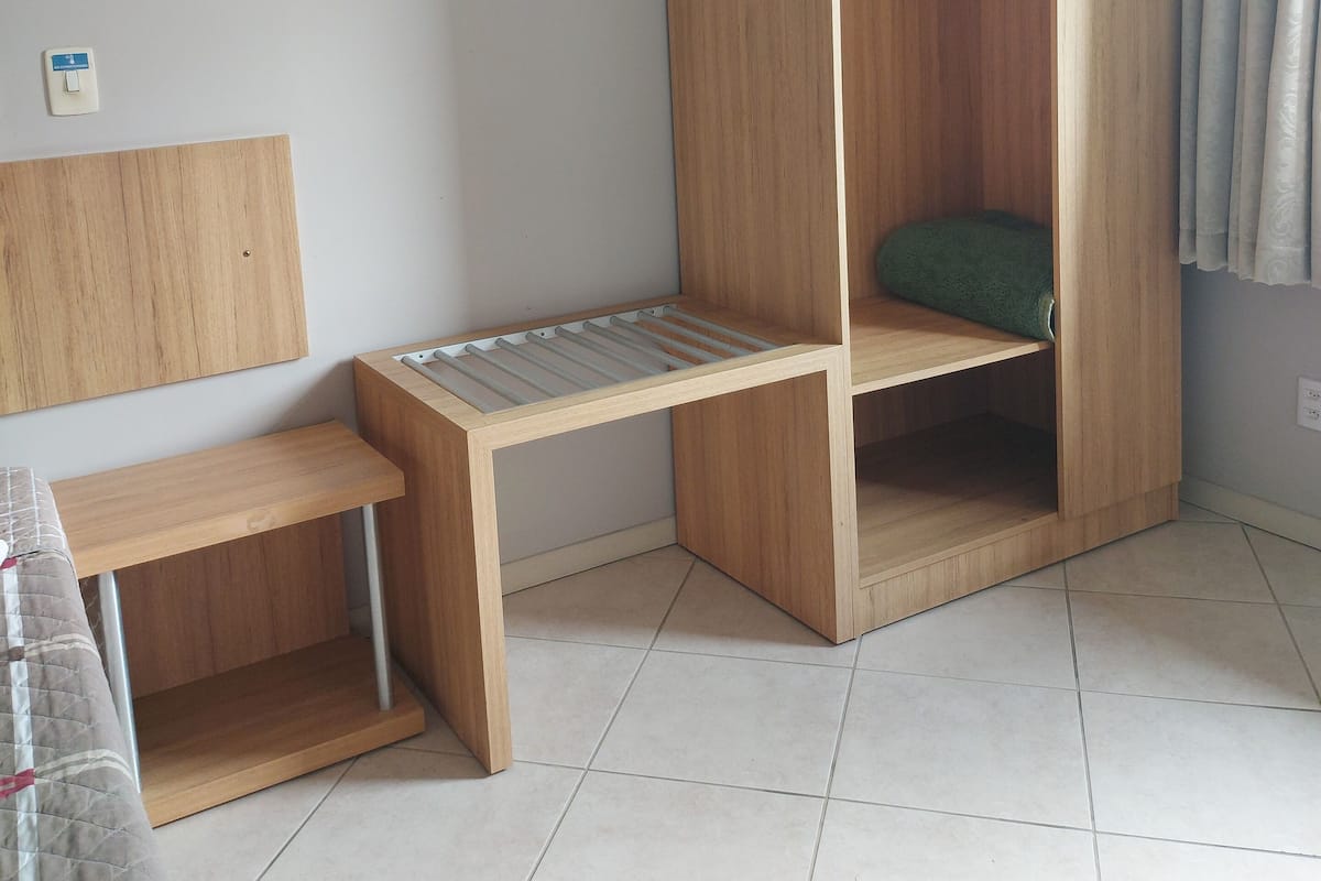 A room with a wooden bed, a small wooden bench, and a tiled floor.