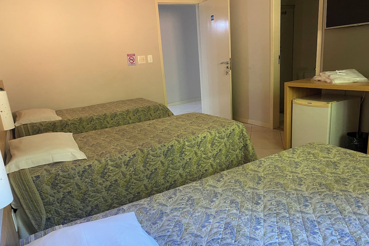A hotel room with two beds, a small desk, a refrigerator, and a door leading to a bathroom.