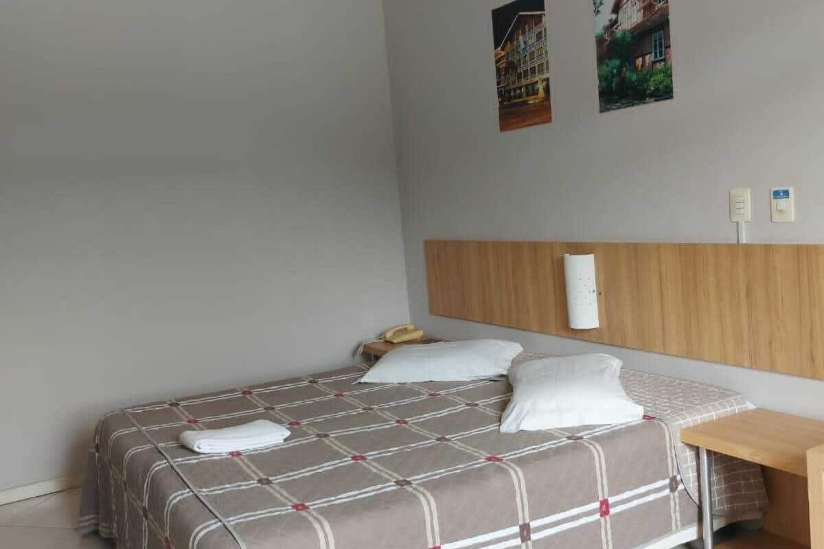 A hotel room with a bed, a wooden headboard, a bedside table, and two wall-mounted light fixtures.