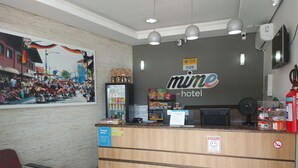 A hotel reception desk with a sign for 'mine hotel', a refrigerator stocked with beverages, a vending machine, and a fire extinguisher. - Hotel Mime (Blumenau)