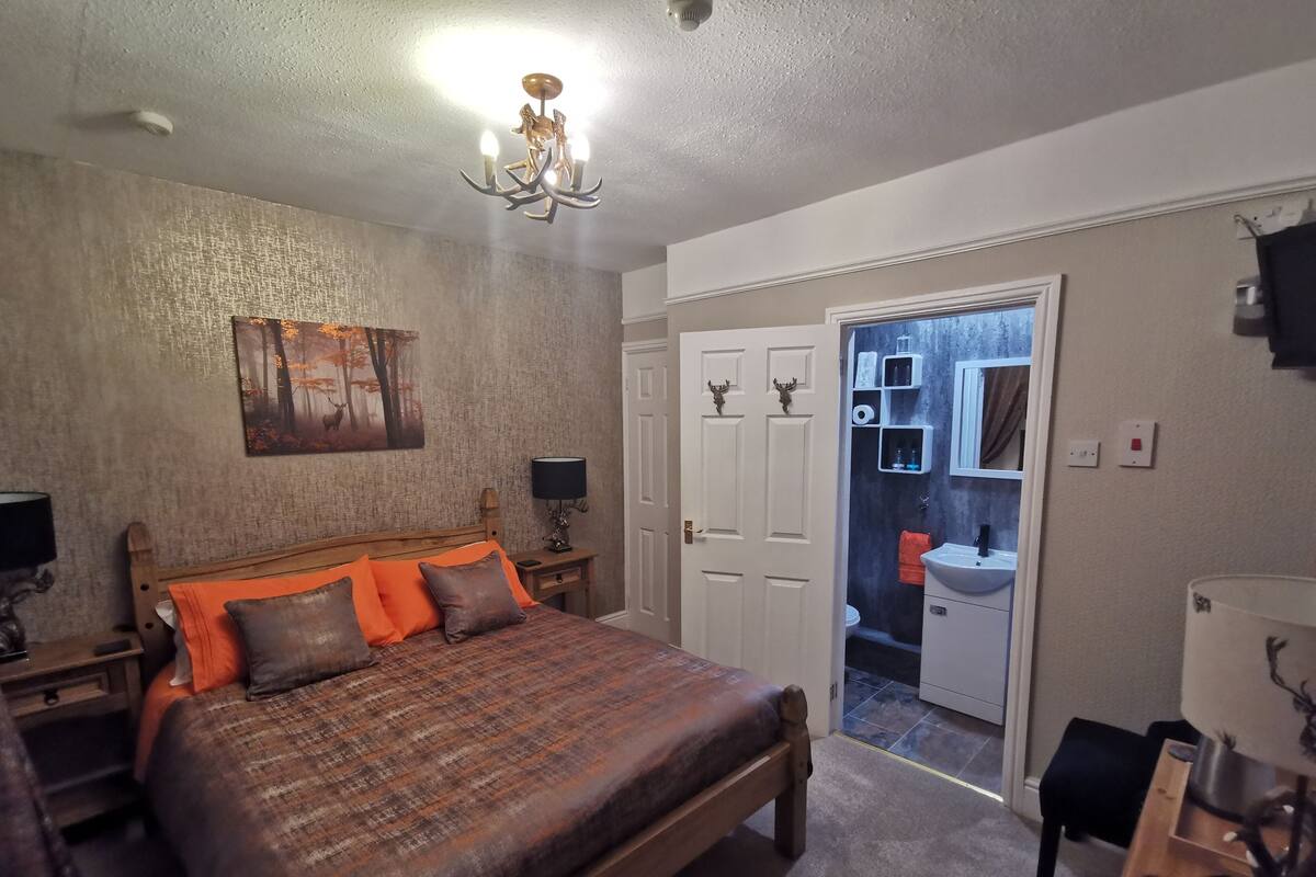 A bedroom with a large bed, a nightstand, a lamp, a painting, and a door leading to a bathroom.