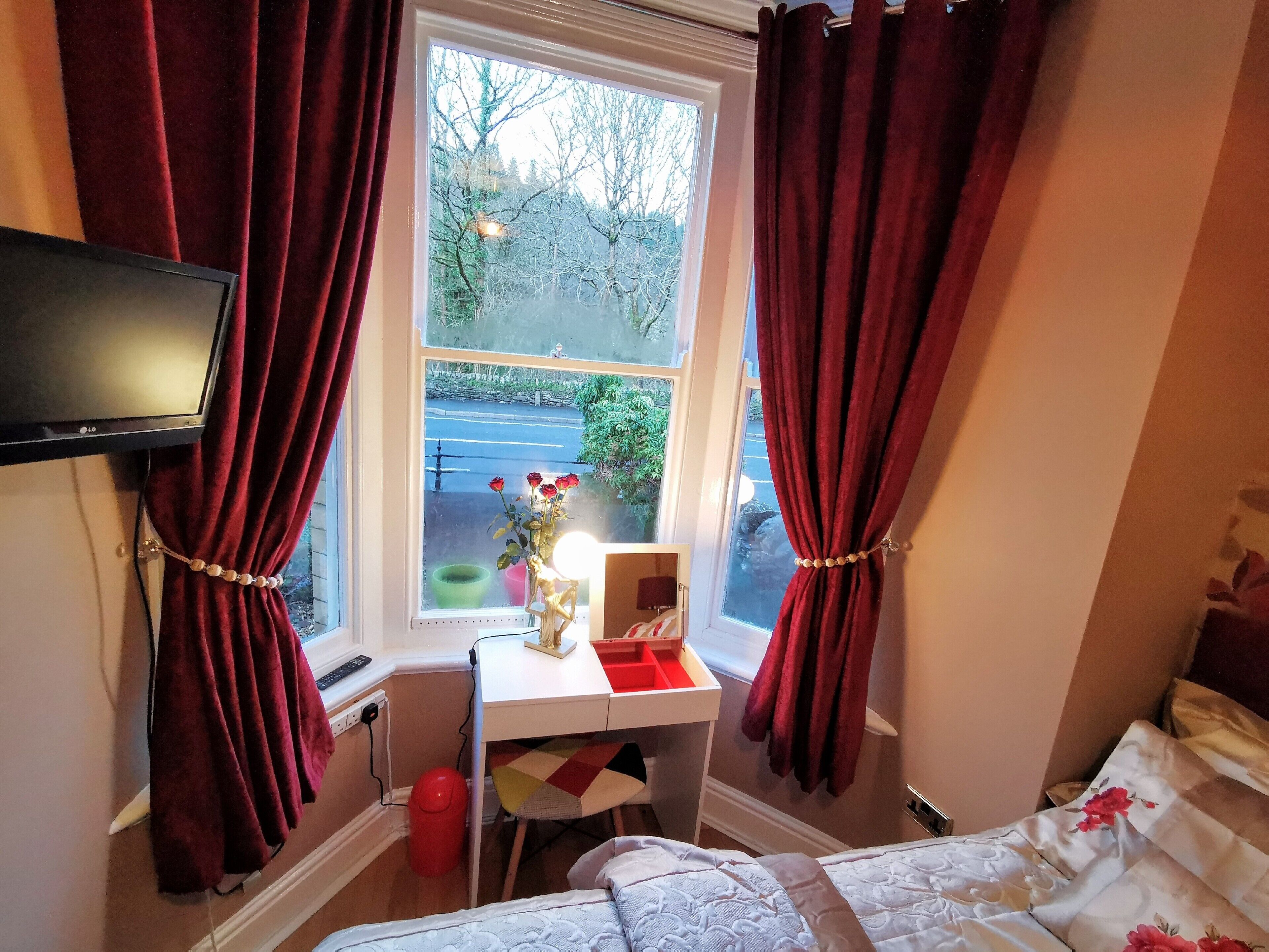 A bedroom with a bed, a desk with a chair, a TV, and a window with curtains.
