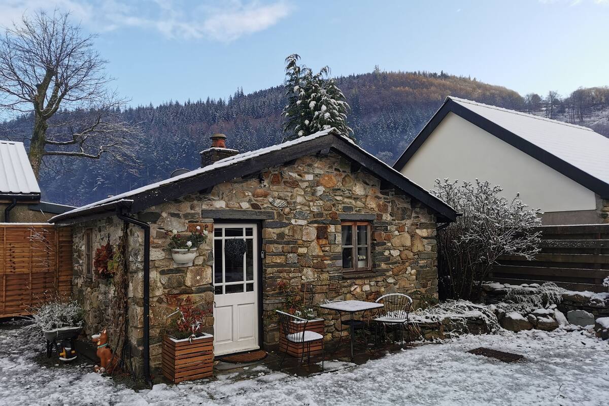 A stone cottage with a white door, a small window, and a wooden fence.