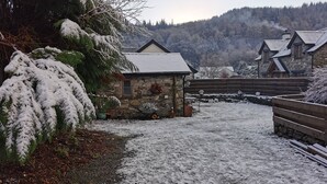Edifici de pedra amb un teulat cobert de neu, envoltat de tanques de fusta i arbres carregats de neu.