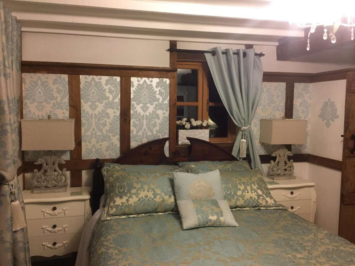 Une chambre à coucher avec un lit, deux tables de chevet, un miroir et une fenêtre avec des rideaux.