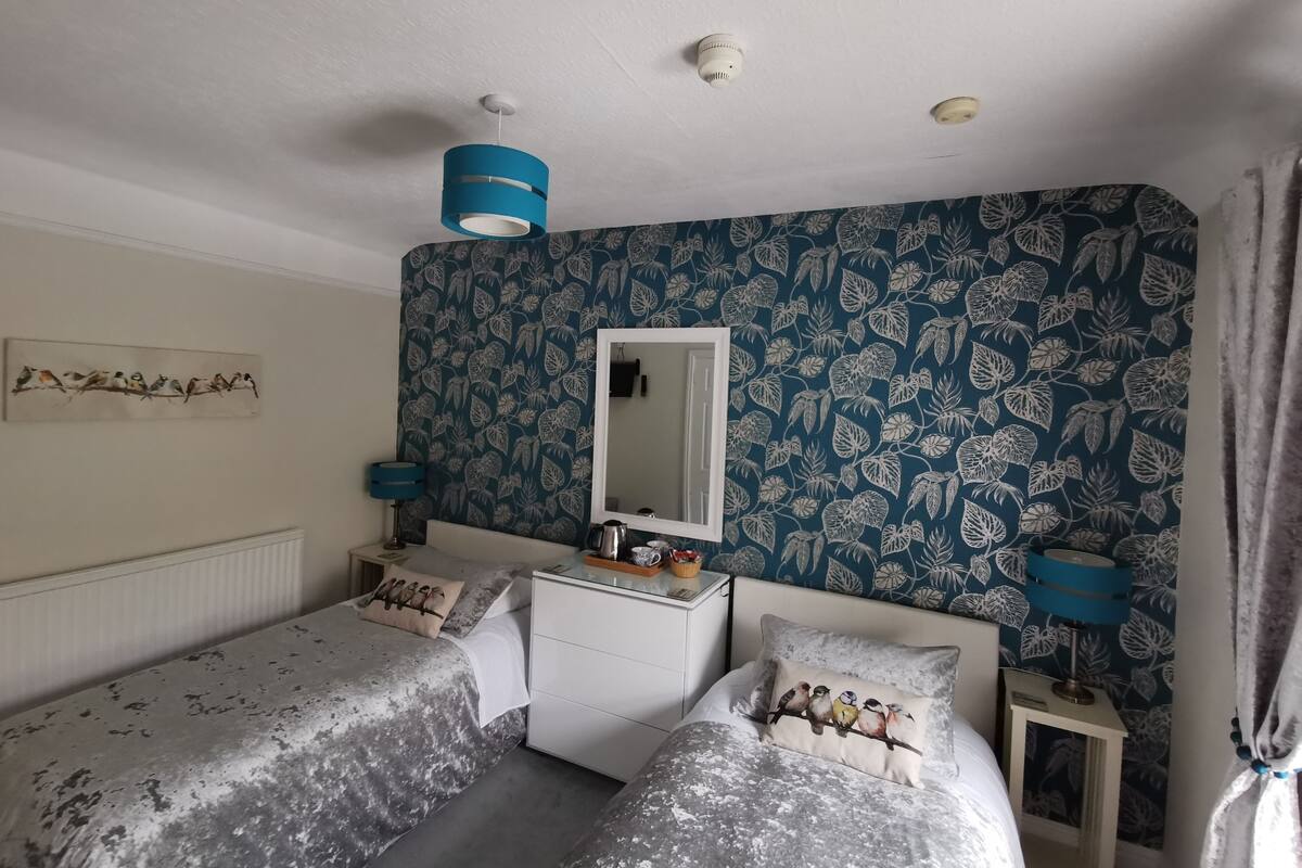 A bedroom with two beds, a dresser, a mirror, and a floral-patterned wall.