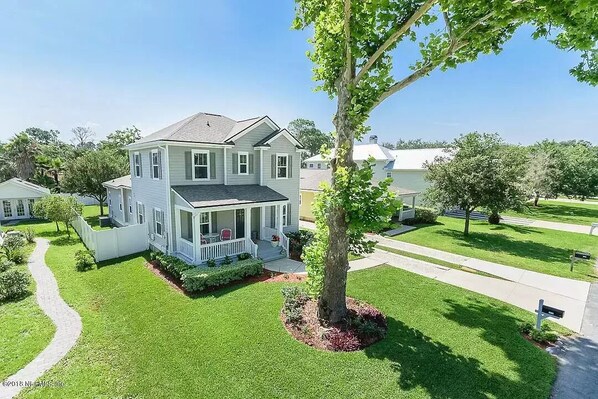 A two-story house with a porch, surrounded by well-maintained lawns and trees.