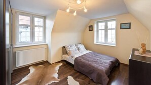 A bedroom with a sloped ceiling, a bed with patterned bedding, a cowhide rug, a radiator, and a desk with a vase. - Gdańskie Apartamenty Gdańskie Poddasza (Gdansk)