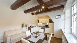 A compact living space with a kitchenette, a dining area with a table and chairs, and a sofa. - Gdańskie Apartamenty Gdańskie Poddasza (Gdansk)