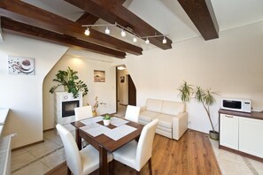 A dining area with a wooden table and white chairs, a white sofa, and a microwave on a cabinet. - Gdańskie Apartamenty Gdańskie Poddasza (Gdansk)