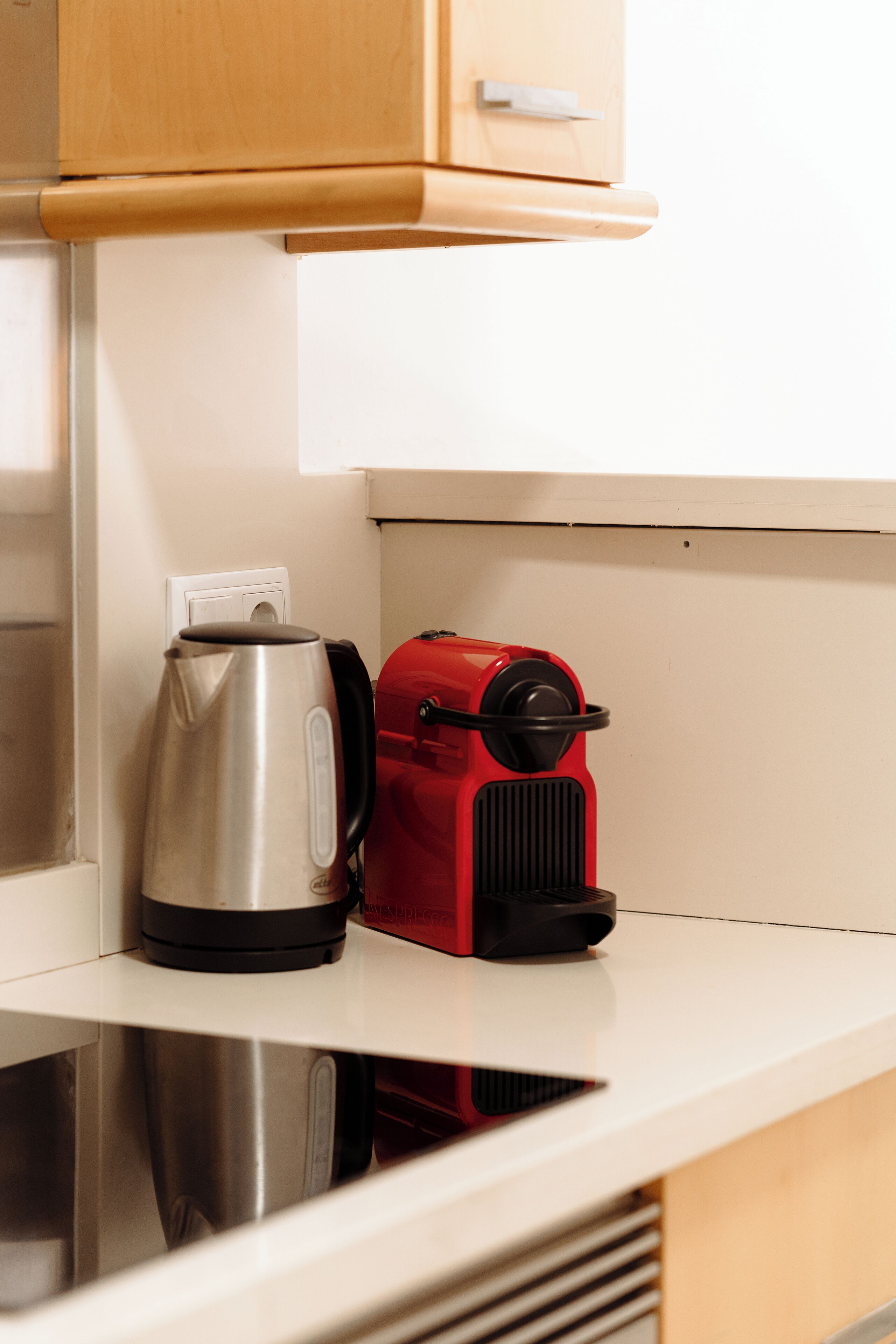 Una cocina con un hervidor de acero inoxidable y una cafetera roja sobre una encimera blanca.