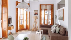 Ein Wohnzimmer mit einem braunen Sofa, einem weißen Tisch und einem Fernseher auf einem Holzboden.