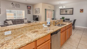 A kitchen with granite countertops, wooden cabinets, a dishwasher, and a dining area with a table and chairs. - Paradise Palms-ru1074 (Kissimmee)
