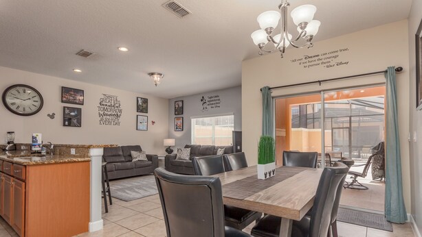 A modern kitchen with a granite countertop, a built-in oven, and a coffee maker. There is a dining area with a wooden table and chairs, and a living room with a sofa and a coffee table. - Paradise Palms-ru1074 (Kissimmee)