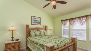 A bedroom with a wooden bed, two bedside tables, a ceiling fan, and a window with curtains. - Windsor Palms-ru1025 (Kissimmee)