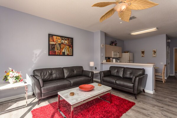 A modern living room with two leather sofas, a red rug, and a ceiling fan.