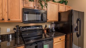 A kitchen with wooden cabinets, a black microwave, a stainless steel refrigerator, a stove, and a blender. - Terra Verde-ru1056 (Kissimmee)