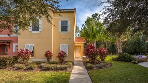 A two-story building with a yellow facade, white shutters, and a red-tiled roof. A concrete pathway leads to the entrance. - Terra Verde-ru1056 (Kissimmee)