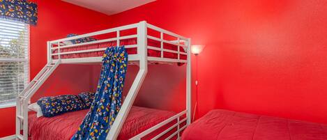 A bunk bed room with a red wall, a window with blinds, and a white ladder.