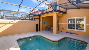 Una piscina con un recinto in vetro, un patio con sedie e vista sugli edifici circostanti.