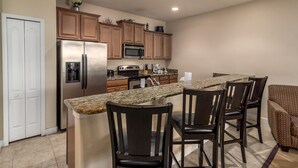 Una cucina con piano di lavoro in granito, elettrodomestici in acciaio inossidabile, mobili in legno e un angolo con sedute.