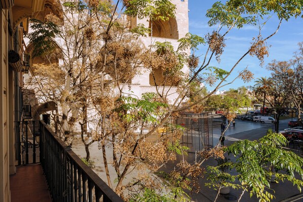Un balcón con vista a una calle, árboles y un edificio con arcos.