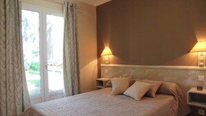 A bedroom with a bed, two bedside tables, a nightstand, a window with curtains, and a wall-mounted lamp.