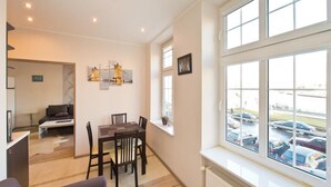 A modern living room with a dining area, large windows with a view of a parking lot, and a cozy seating area. - Gdańskie Apartamenty Targ Rybny Mołtawa (Gdansk)
