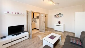 A modern living room with a flat-screen TV, a white sofa, a coffee table, and a small white cabinet. - Gdańskie Apartamenty Targ Rybny Mołtawa (Gdansk)