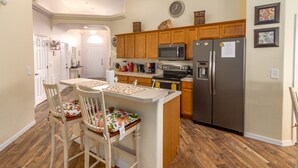 Une cuisine avec des meubles en bois, un réfrigérateur en acier inoxydable, un four à micro-ondes et une cuisinière. On y trouve également un petit îlot central avec des chaises et une table.