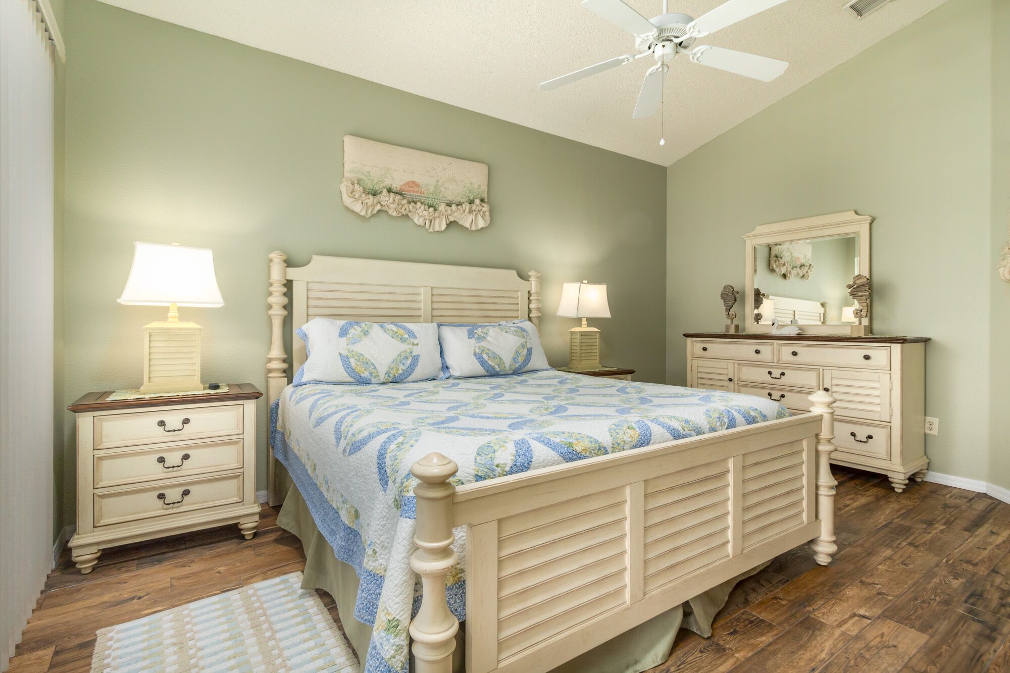 A bedroom with a bed, nightstands, a dresser, a ceiling fan, and a mirror.
