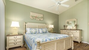 Une chambre à coucher comprenant un lit, des tables de chevet, une commode, un ventilateur de plafond et un miroir.