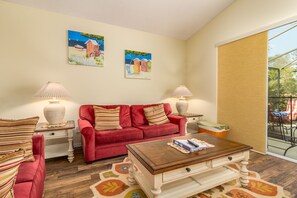 A cozy living room with a red sofa, two side tables with lamps, and a wooden coffee table. There are two paintings on the wall and a large window with a view of the outdoors. - Glenbrook Resort-ru464 (Clermont)