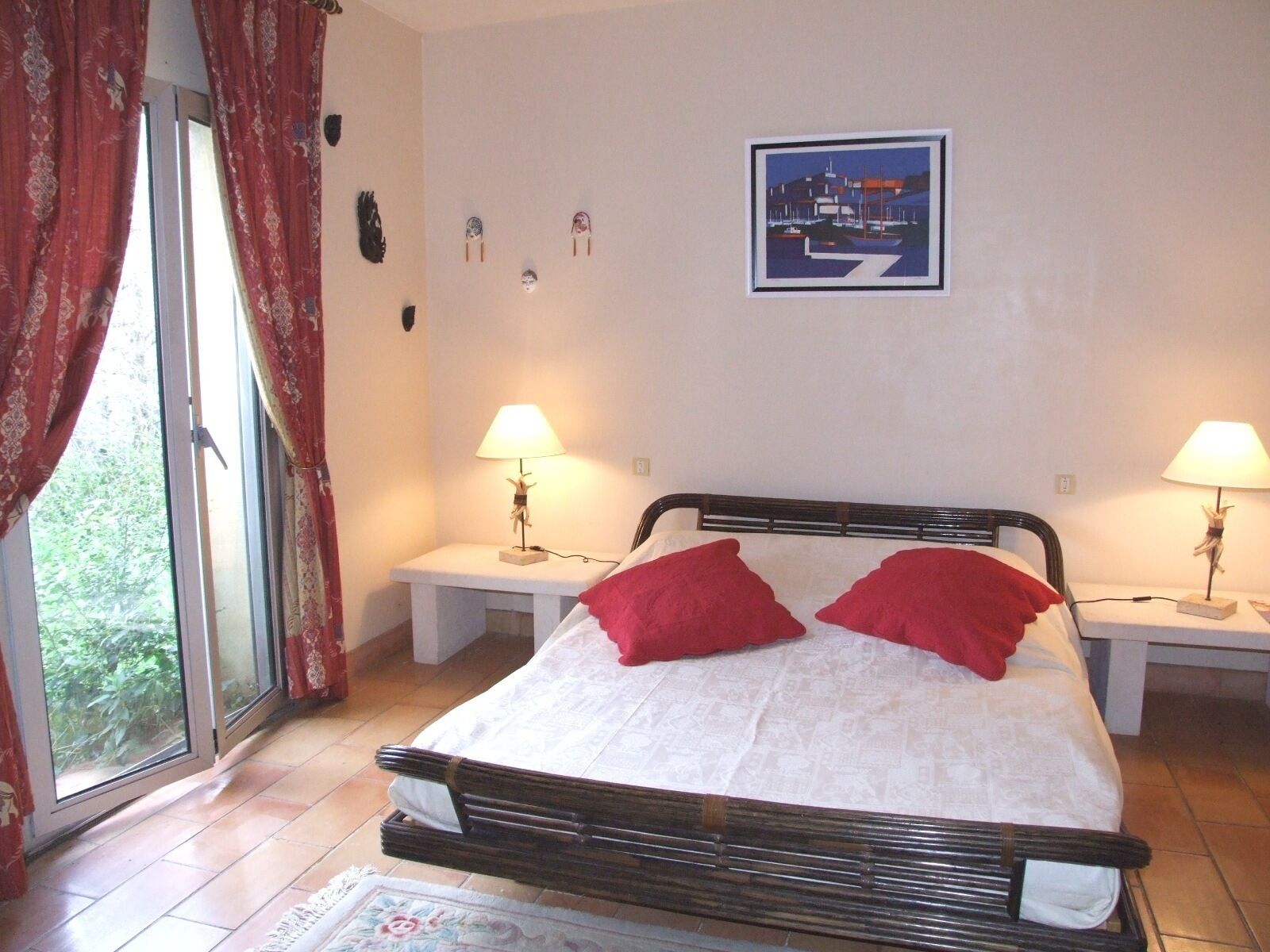 A bedroom with a bed, two bedside tables, a window with curtains, and a wall-mounted picture.