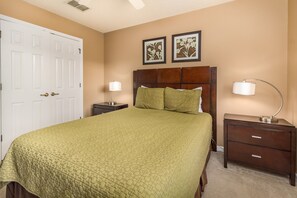Une chambre à coucher comprenant un lit, deux tables de chevet, une commode, une porte et deux tableaux floraux encadrés accrochés au mur.