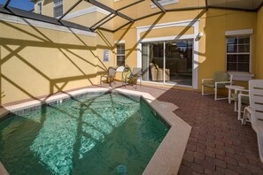 Une piscine dont le bord est revêtu de carrelage, entourée d’une terrasse dallée en briques et agrémentée de mobilier d’extérieur blanc.