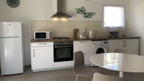 Une cuisine moderne équipée d’un réfrigérateur, d’un four à micro-ondes, d’une cuisinière, d’un four et d’un lave-linge. On y trouve une table à manger avec des chaises et une horloge murale décorative.
